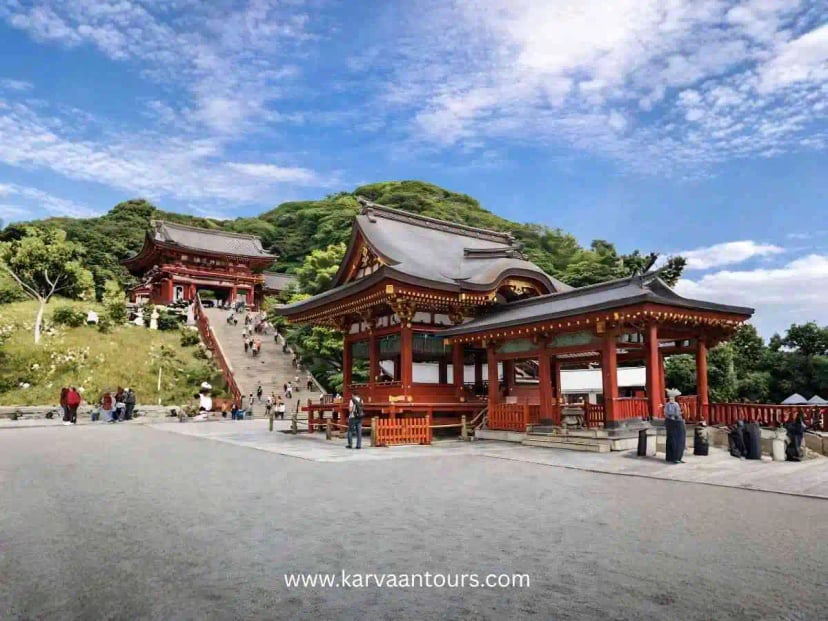 Visitors walking up stone steps between traditional red shrine buildings in Kamakura Japan
