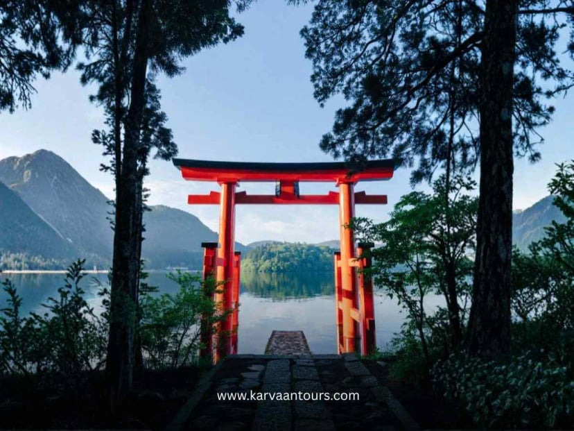 Red torii gate of Hakone Shrine standing by Lake Ashi surrounded by trees and calm water scenery