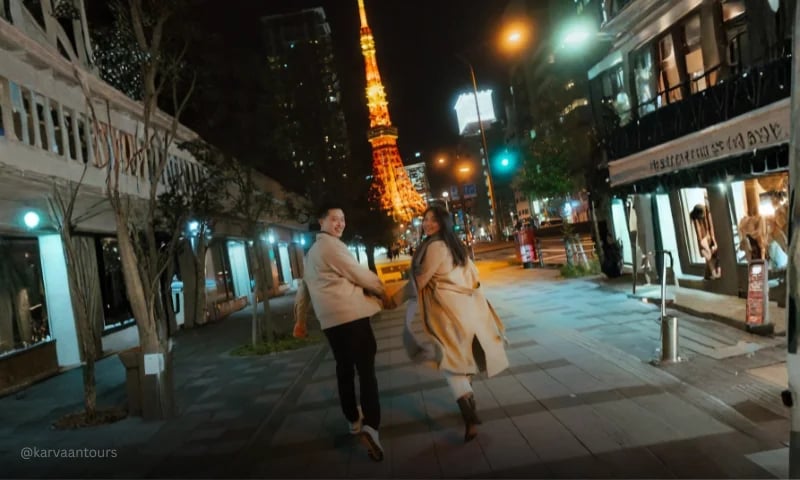 Couple walking through Tokyo streets at night with Tokyo Tower glowing in the background