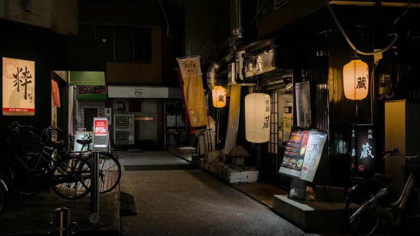 Atmospheric narrow Japanese alleyway illuminated by traditional glowing paper lanterns outside local izakaya storefronts.