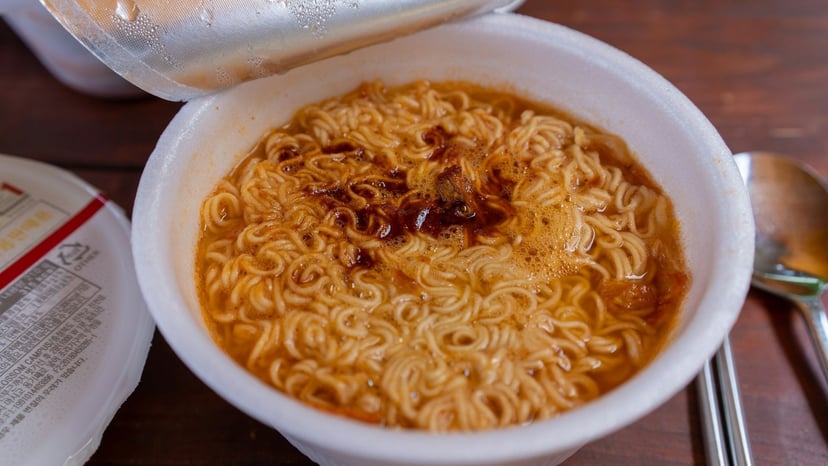 Close-up view of freshly prepared hot instant cup ramen noodles with savory broth and chili oil topping.