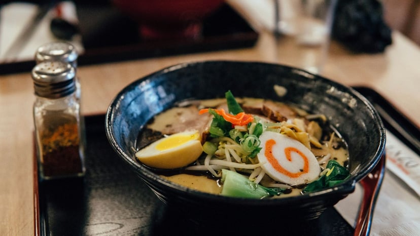 A black ceramic bowl of Japanese ramen topped with a soft-boiled ramen egg, narutomaki fish cake, scallions, bean sprouts, and chashu pork.