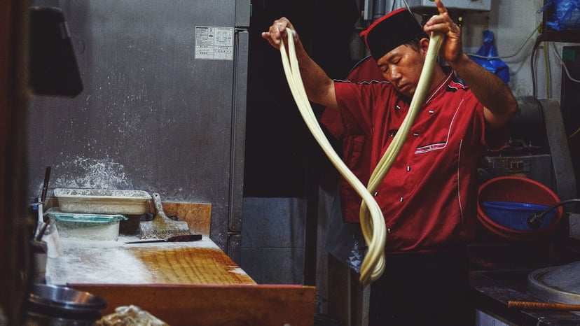 A skilled Japanese chef stretching dough to make fresh hand-pulled ramen noodles in an authentic kitchen setting.