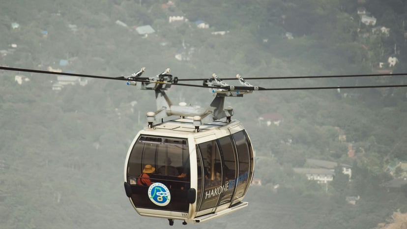 Close-up of a white aerial ropeway gondola cabin carrying passengers over hazy mountain scenery.
