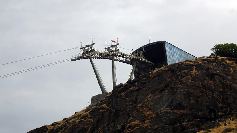 Industrial cable car terminal building perched high on a rocky mountain cliff with mechanical support towers.