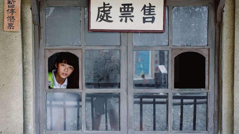 A traditional wooden glass ticket booth window with Kanji signage showing a staff member inside.