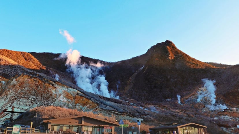 Sulfurous volcanic mountain slopes with white steam billows rising during warm sunset light at Owakudani.
